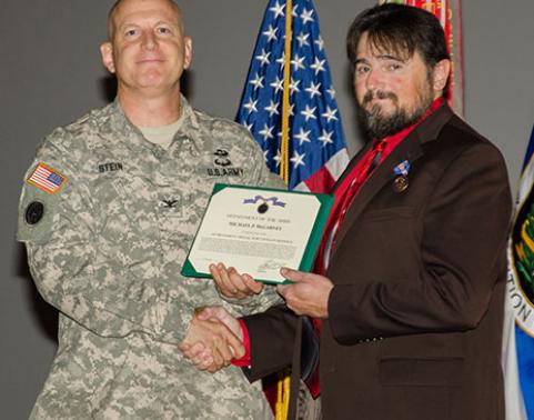 Man hands award to another man while shaking hands.